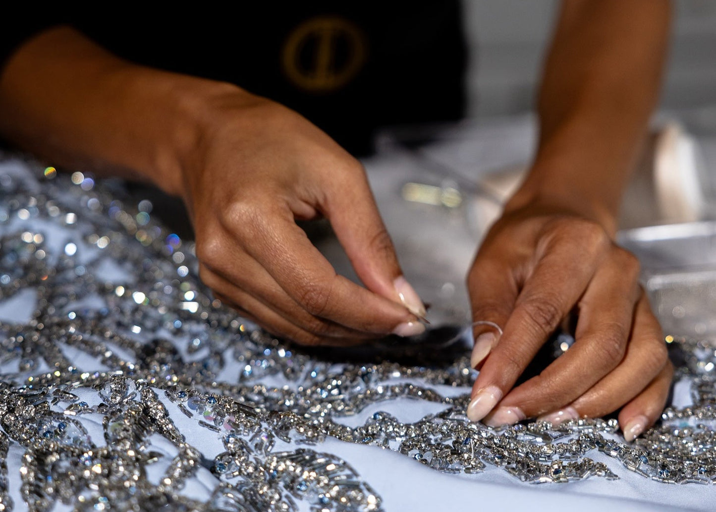 Close-up of hands working with silver sequins on a dark background