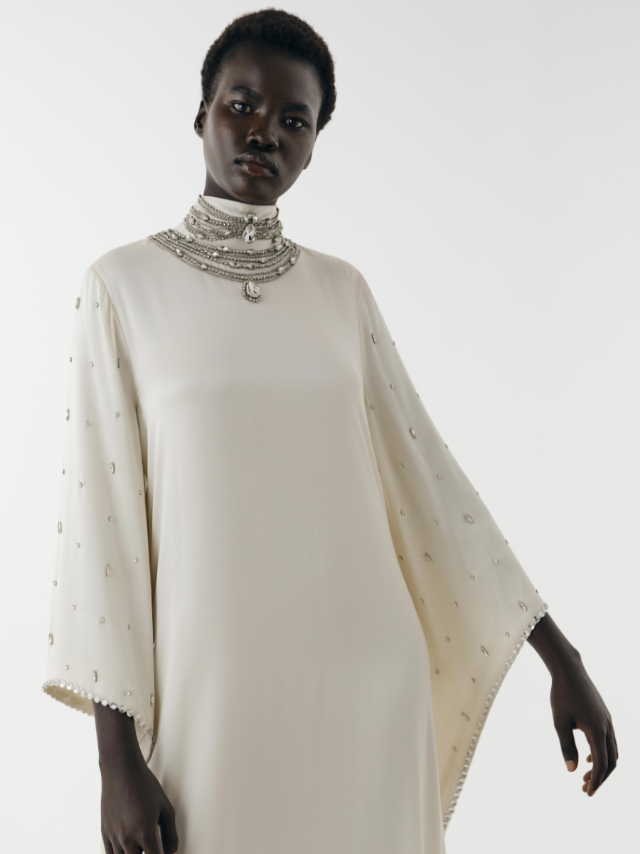 Person wearing a white garment with intricate detailing on a plain background