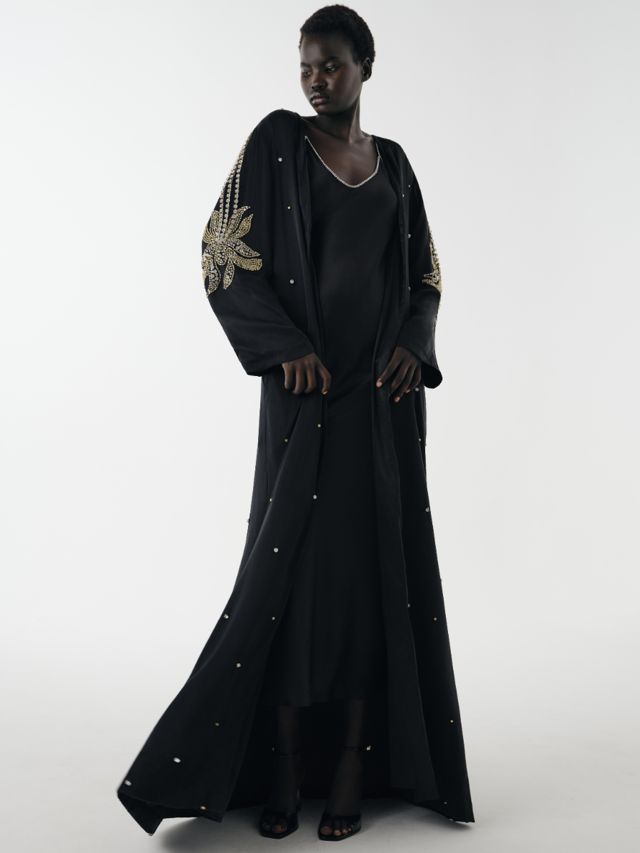 Woman wearing a black dress with gold embellishments on a white background