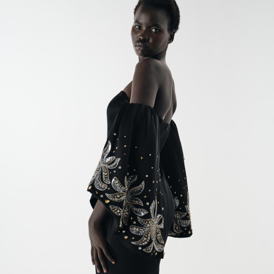 Woman wearing a black off-shoulder top with intricate white embroidery on a white background