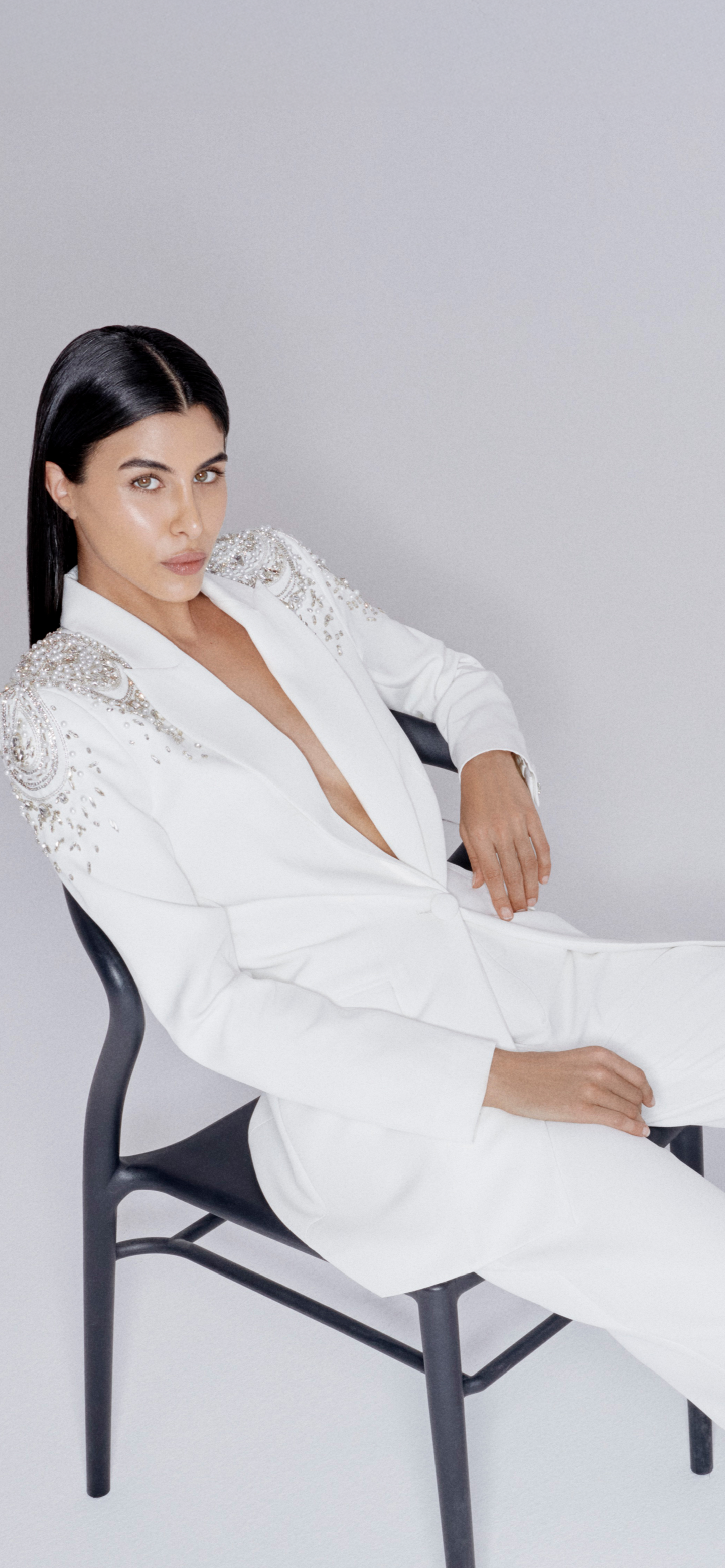 Person wearing a white suit sitting on a chair against a plain background