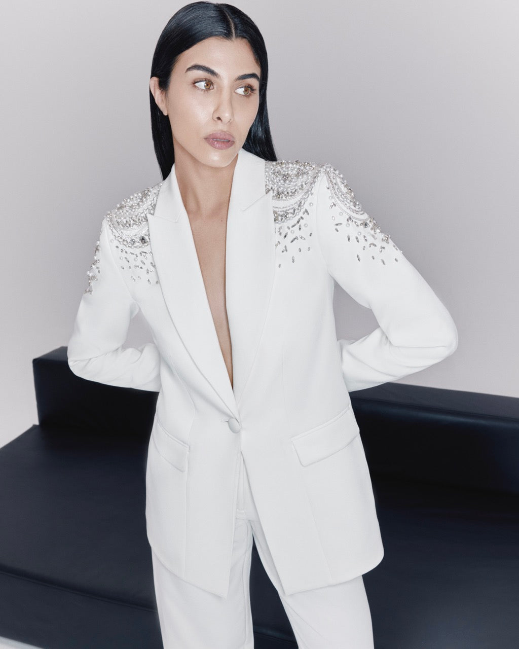 Woman wearing a white blazer with embellishments on a plain background